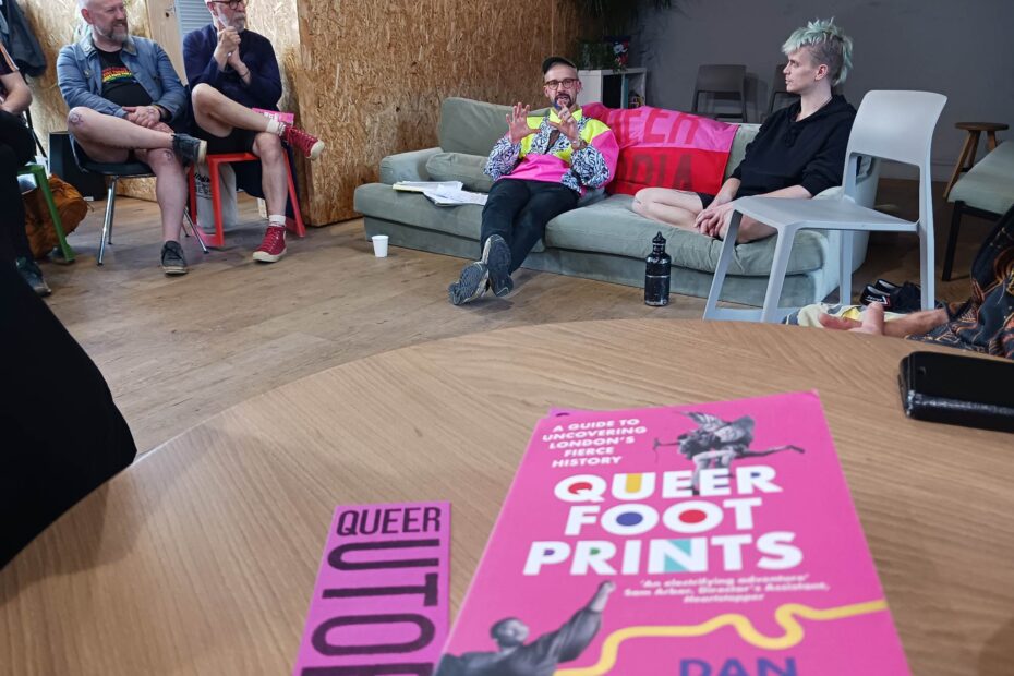 Dan and Lip are sitting on sofas for the Queer Footprints Q&A. There is a copy of Dan's book with a Queer Utopia bookmark next to it on a table.