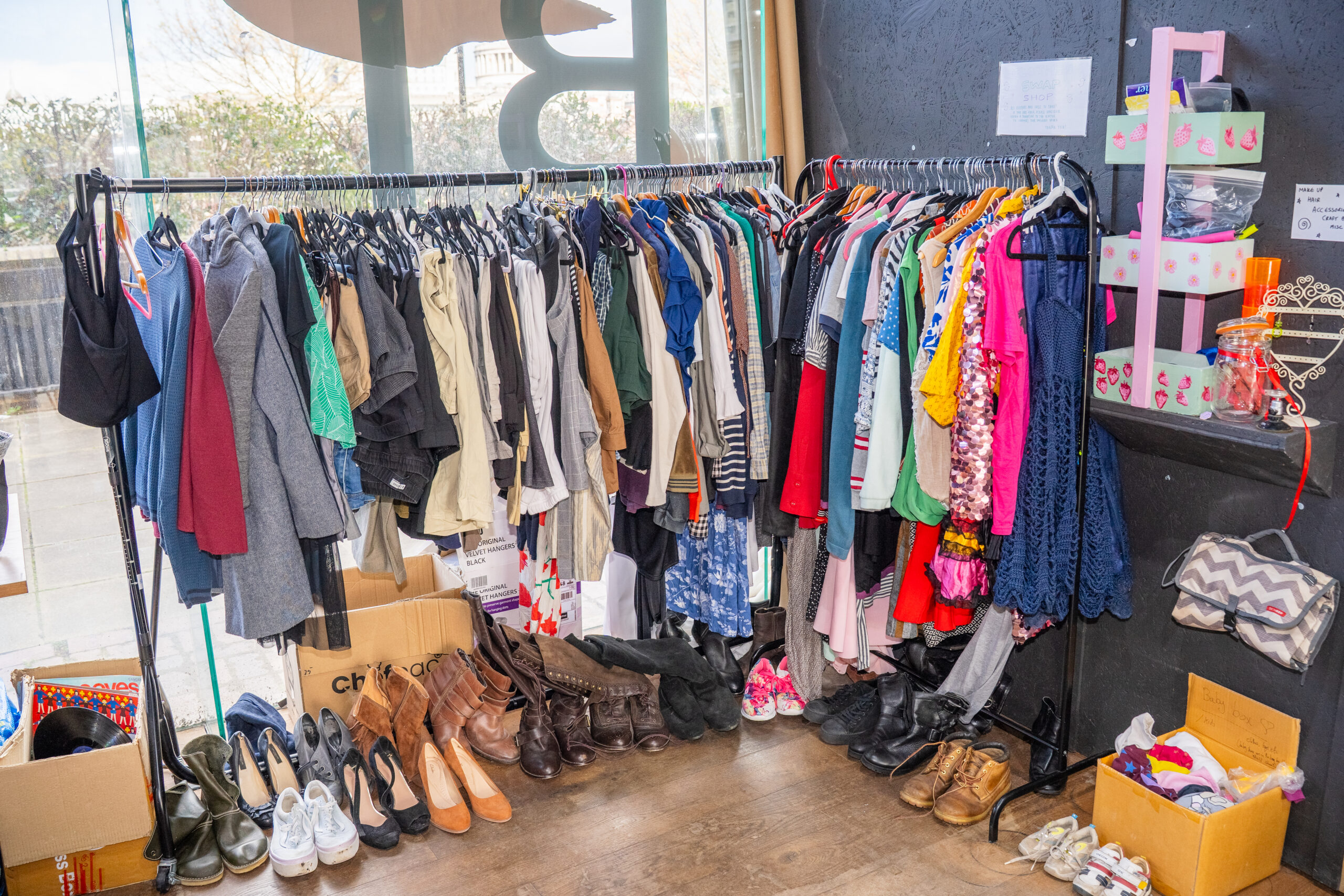 Clothes rails filled with colourful items. Shoes are lined up under the rails.