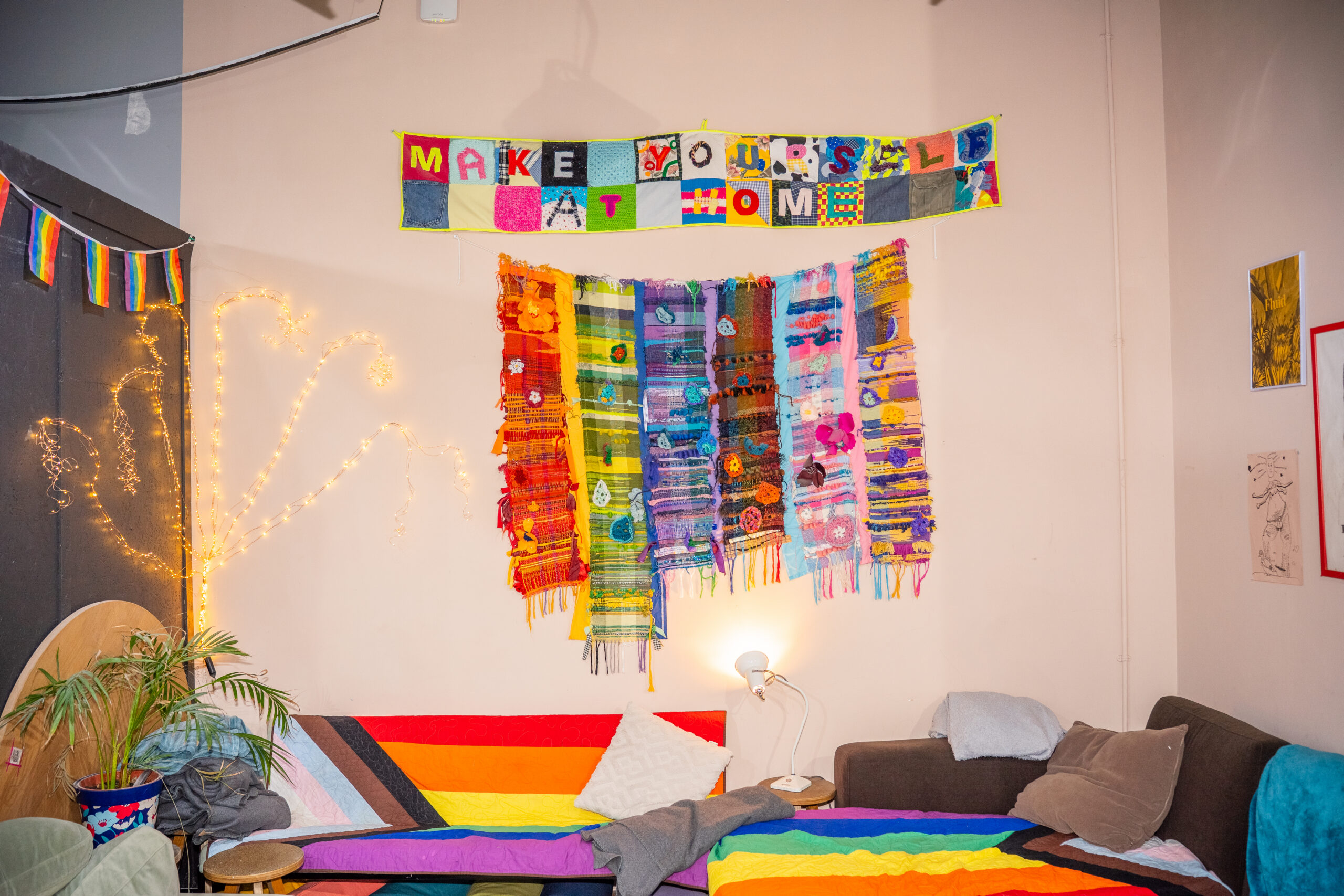 Make yourself at home crochet banner with sofas with rainbow throws below.